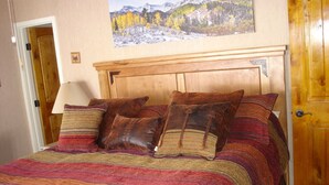 Un lit avec une tête de lit en bois, plusieurs oreillers et une couverture rayée aux couleurs vives.