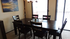 Un coin repas avec une table en bois foncé, six chaises et un tableau représentant un paysage de montagne accroché au mur.