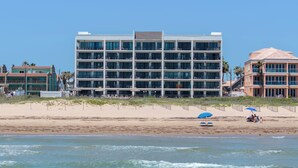 A beachfront hotel with multiple floors, a sandy beach in front, and a clear blue sky. - Experience the Island at our  Paradise Palm - Condo 304, a 2BR retreat in South Padre Island. (South Padre Island)