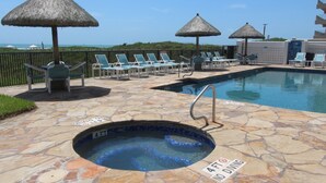 A pool area with lounge chairs, a hot tub, and thatched umbrellas. - Experience the Island at our  Paradise Palm - Condo 304, a 2BR retreat in South Padre Island. (South Padre Island)