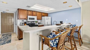 A kitchen with wooden cabinets, a microwave, a stove, and a breakfast bar with wicker chairs. - Experience the Island at our  Paradise Palm - Condo 304, a 2BR retreat in South Padre Island. (South Padre Island)