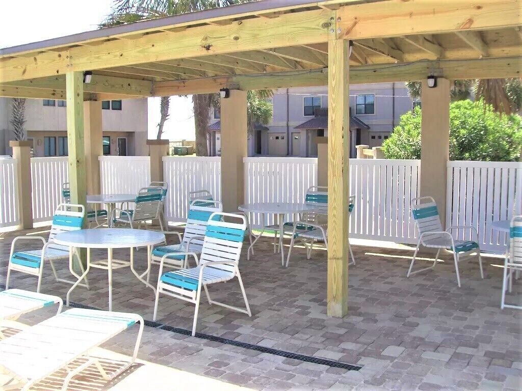 An outdoor patio area with tables and chairs, a wooden pergola, and a white fence.