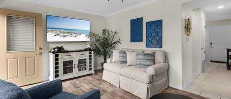 A living room with a beige sofa, a blue armchair, a coffee table, a TV, and a ceiling fan.