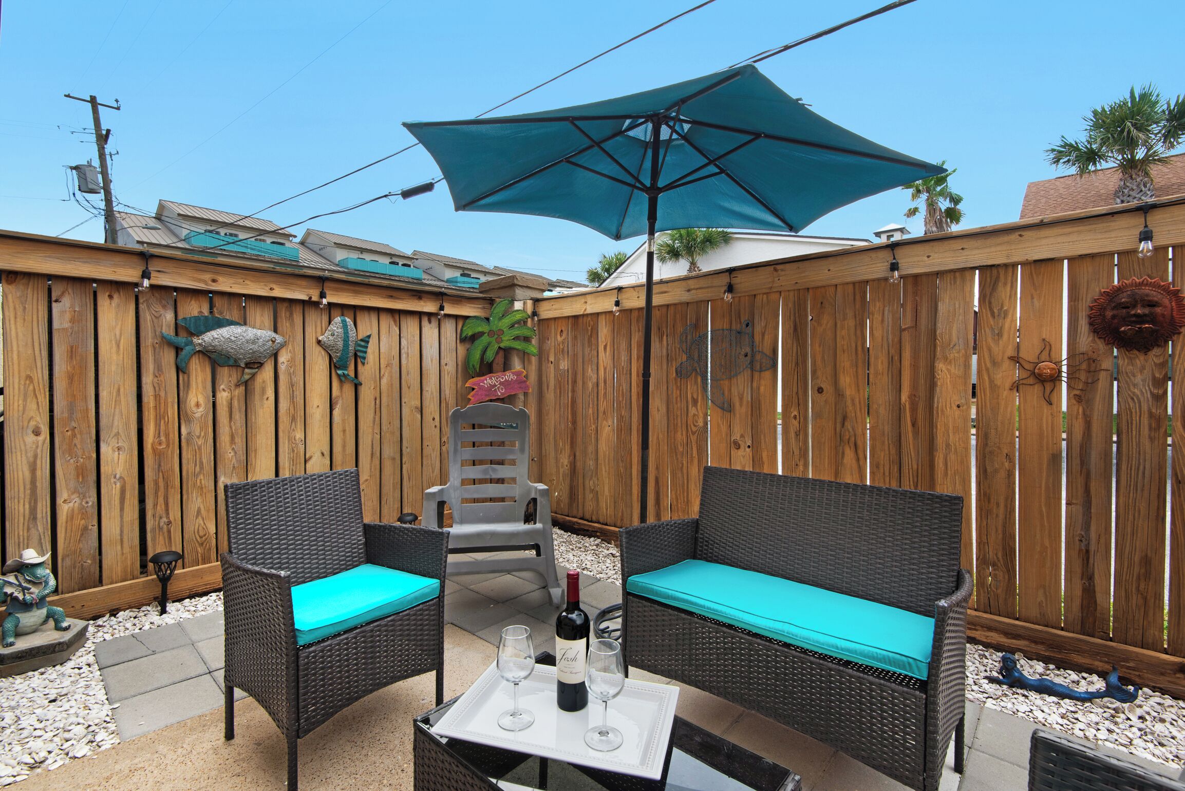 Une terrasse avec des meubles en osier, une table avec une bouteille et des verres, et un parasol bleu.
