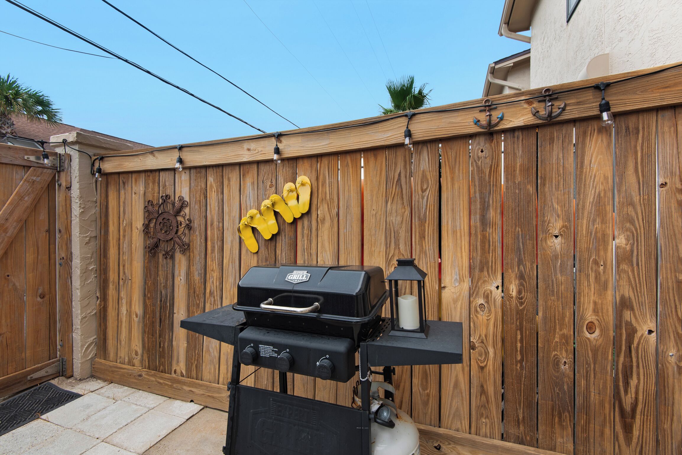 A backyard with a wooden fence, a barbecue grill, and a lantern.