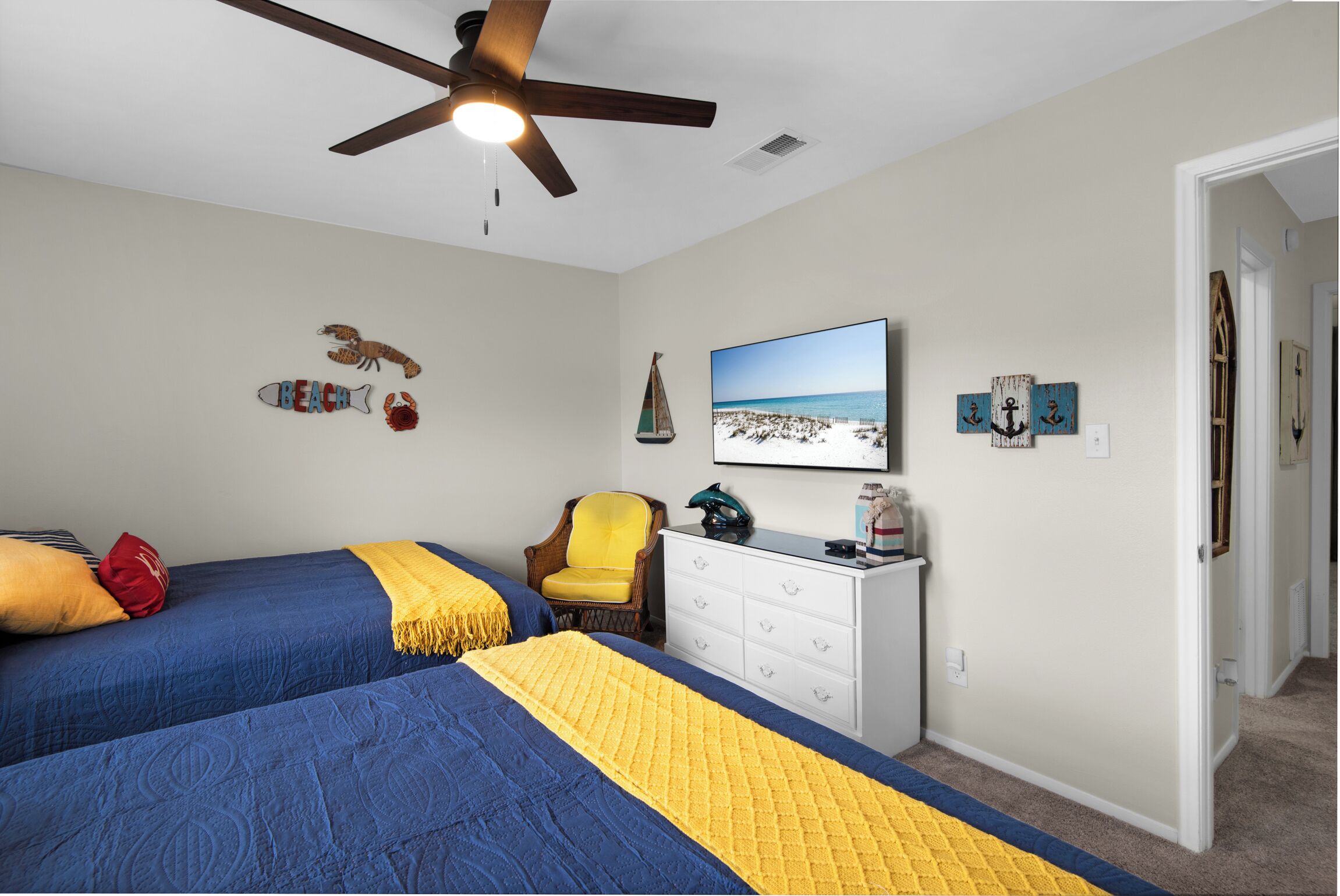 A bedroom with two beds, a ceiling fan, a TV, and wall decorations.