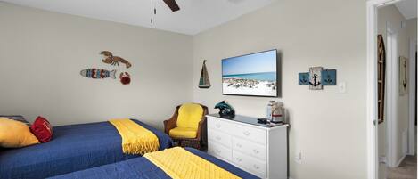 A bedroom with two beds, a ceiling fan, a TV, and wall decorations.