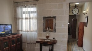 A room with a television on a wooden cabinet, a mirror on the wall, a table with a glass and a decorative item, and a patterned floor.