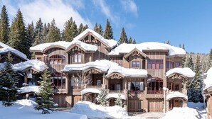 Un gran lodge de varios pisos con fachada de madera y techos cubiertos de nieve, rodeado de árboles nevados.