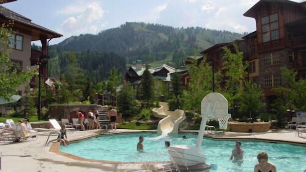 Uma área de piscina com escorregador, espreguiçadeiras e montanhas ao fundo.
