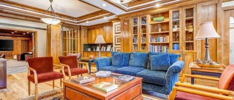 A spacious library with wooden bookshelves, a blue sofa, and red chairs.