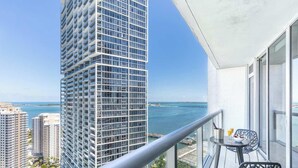 A balcony with a clear view of a tall building, a body of water, and a distant bridge. - Riverwalk Chic Suite | Brickell's High Walk Score (Miami)