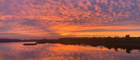 A sunset over a calm lake with a distant shoreline and a clear sky.
