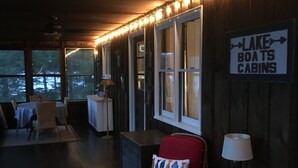 A cozy cabin interior with a dining area, a sign indicating 'Lake Boats Cabins', and a view of the outdoors. - Charming Lakefront Cottage - Northern Lake George (Ticonderoga)