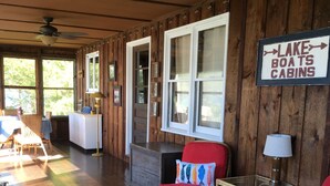 A cabin interior with a wooden floor, wicker furniture, and a sign indicating 'Lake Boats Cabins'. - Charming Lakefront Cottage - Northern Lake George (Ticonderoga)