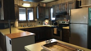 A modern kitchen with wooden cabinets, a stainless steel refrigerator, a built-in oven, and a wooden countertop with a sink. - Charming Lakefront Cottage - Northern Lake George (Ticonderoga)
