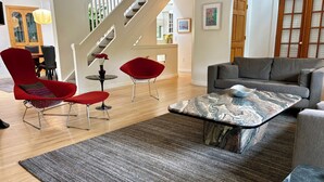 Un salon moderne avec un escalier, des fauteuils rouges, un canapé gris et une table basse en marbre.