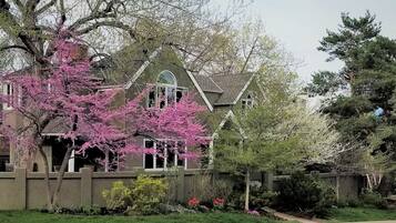 A two-story house with a prominent front porch, a stone wall, and a variety of flowering plants.