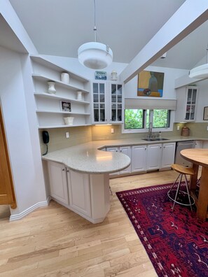 A modern kitchen with white cabinetry, a granite countertop, a built-in island, and a red patterned rug. - Enjoy the Magic of Chautauqua Park & Walk to CU / 4-5 Bedroom Home (Boulder)