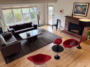 A living room with a sofa, coffee table, red chairs, a fireplace, and a view through the window.
