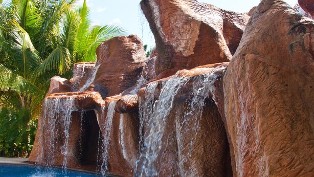 A pool with a waterfall feature surrounded by large rock formations and palm trees.