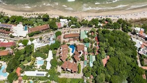An aerial view of a coastal resort with a beach, swimming pool, and lush greenery.