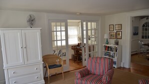 A living room with a white cabinet, striped armchair, and a wicker chair. - Quaint & Cozy Downtown Chatham Home, Walk to Town and Beaches (Chatham)