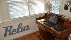 A wooden desk with a laptop, a fan, and a "Relax" sign on the wall. - Quaint & Cozy Downtown Chatham Home, Walk to Town and Beaches (Chatham)