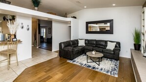 A modern living room with a sectional sofa, a round coffee table, and a large mirror on the wall. - Spacious 3+3 w/ Pool & Game room, 5mins from Lake (Lake Havasu City)