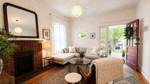 A living room with a fireplace, a sofa, a coffee table, a chair, and a door leading outside. - Historic Craftsman, Walk to Duke (Durham)
