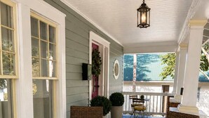 A covered porch with wicker furniture, a dining table with a glass of white wine, and a view of the house. - Historic Craftsman, Walk to Duke (Durham)