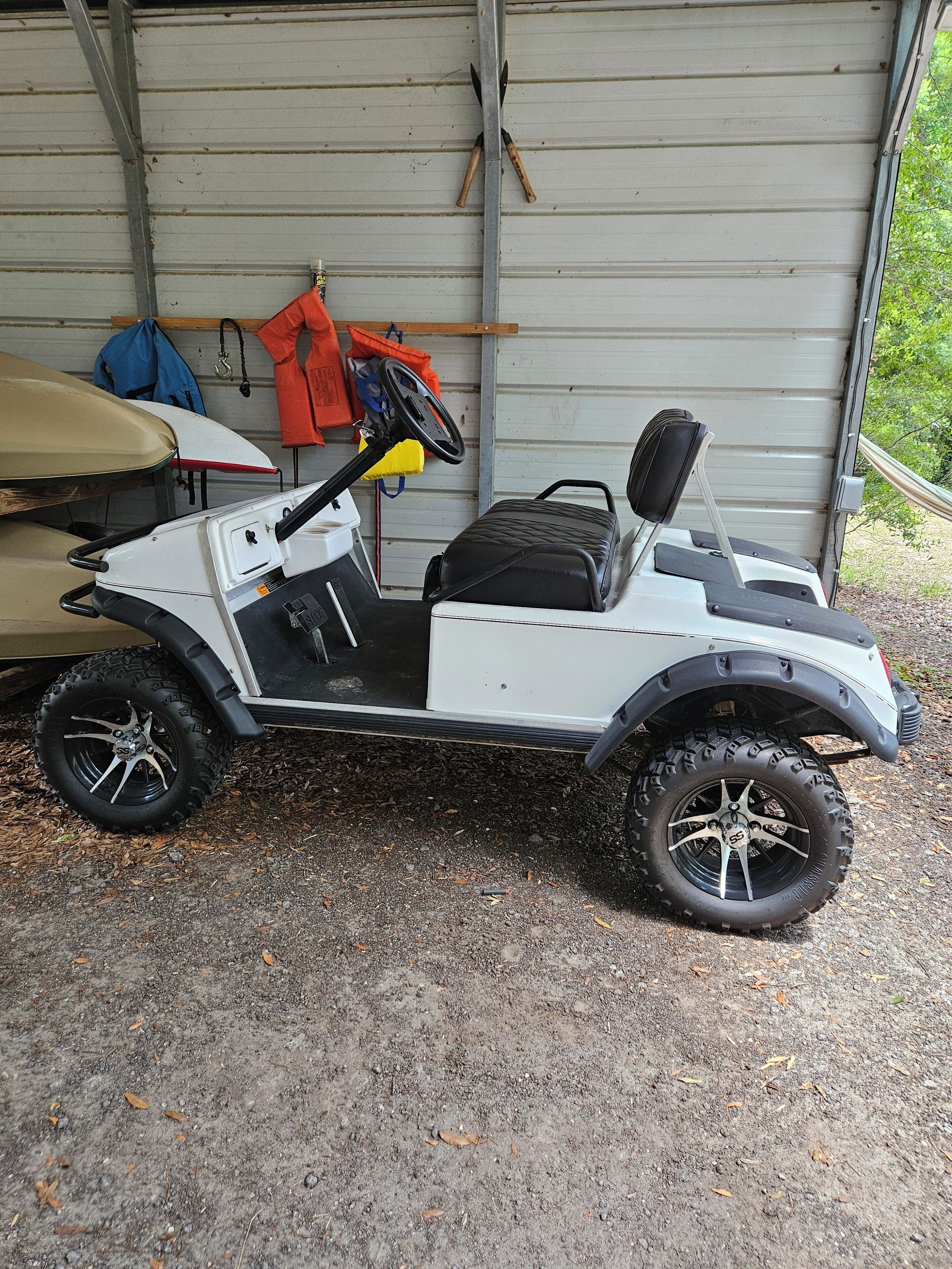 A white golf cart with a black seat and storage compartment, parked outside a garage.