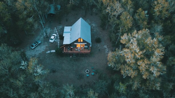 An aerial view of a cabin with a large deck, surrounded by trees.