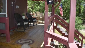 A wooden deck with outdoor furniture, a staircase, and a view of the surrounding forest.