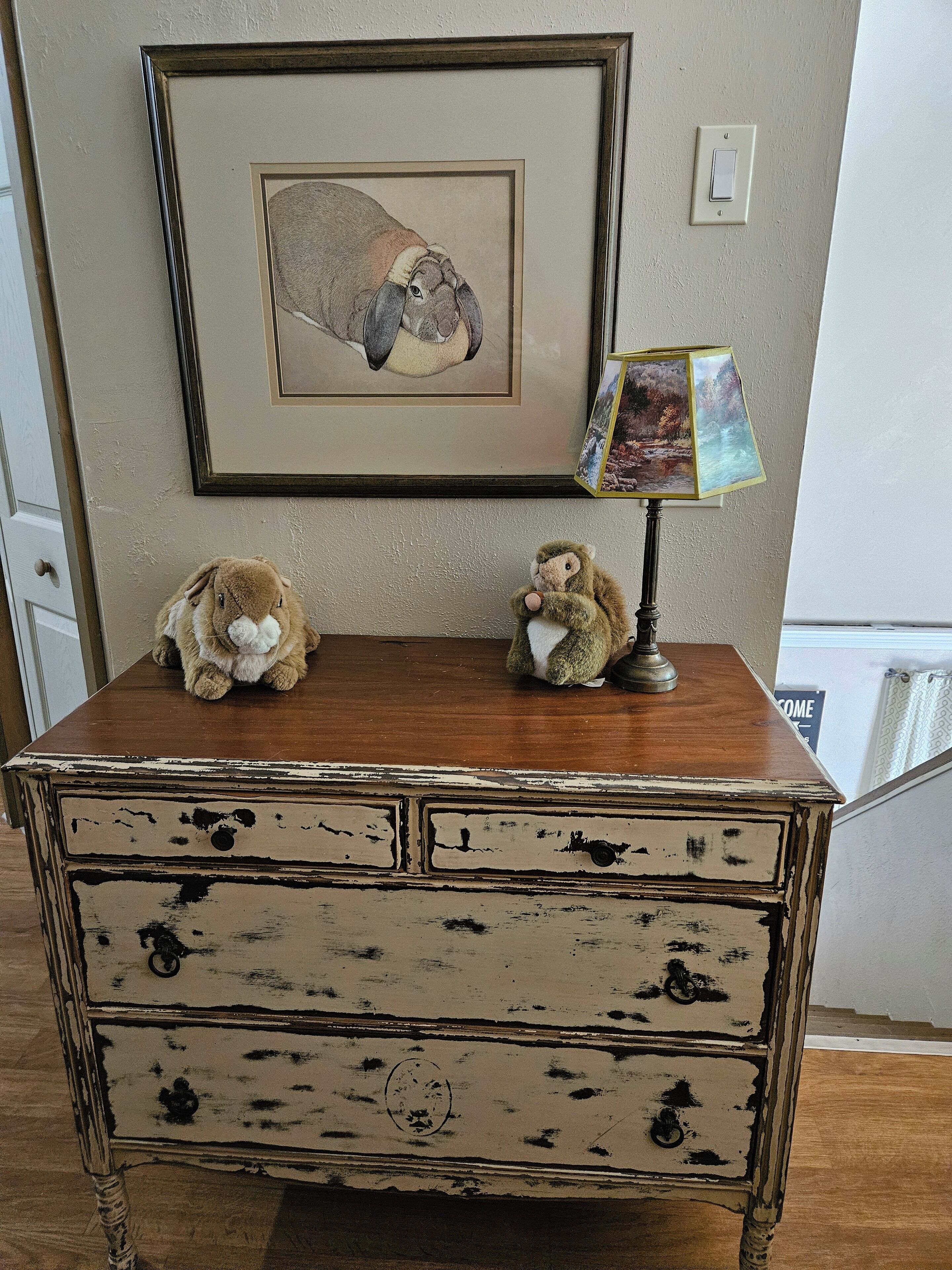 Un aparador de madera con dos peluches, un cuadro enmarcado y una lámpara encima.