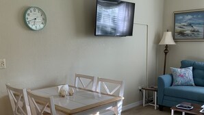 A living room with a dining table, chairs, a TV mounted on the wall, a sofa, and a lamp. - Venetian Vacation! Close To Beaches, Restaurants & Shopping! (Venice)