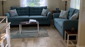 A living room with a blue sofa set, a coffee table, and a ceiling fan. - Venetian Vacation! Close To Beaches, Restaurants & Shopping! (Venice)