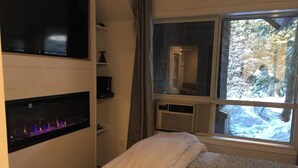 Ein Schlafzimmer mit einem Bett, einem Kamin, einem Fenster mit Blick auf Bäume und einer Heizung.