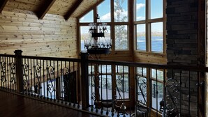 A spacious room with wooden walls and a high ceiling, large windows offering a view of a lake, and a chandelier hanging from the ceiling. - Large Lakefront Paradise on the shores of Lake Michigamme (Champion)