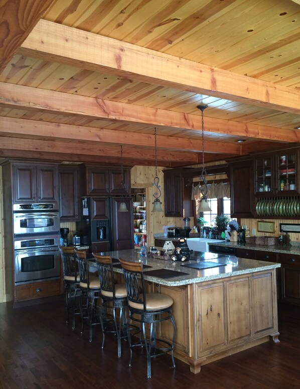 A spacious kitchen with wooden beams, a large island with bar stools, stainless steel appliances, and dark wooden cabinets. - Large Lakefront Paradise on the shores of Lake Michigamme (Champion)