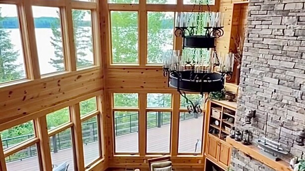A spacious interior with large windows, a stone fireplace, and a wooden ceiling. - Large Lakefront Paradise on the shores of Lake Michigamme (Champion)