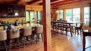 A spacious kitchen with wooden beams, a bar area with stools, and large windows offering views. - Large Lakefront Paradise on the shores of Lake Michigamme (Champion)
