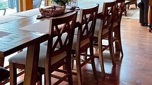 A wooden dining area with a large table and chairs, a chandelier, and large windows with a view of trees. - Large Lakefront Paradise on the shores of Lake Michigamme (Champion)
