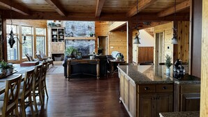 A spacious kitchen with wooden beams, a stone fireplace, and a dining area with a large table and chairs. - Large Lakefront Paradise on the shores of Lake Michigamme (Champion)