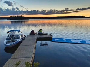 Un quai avec un bateau et un jet ski, une plateforme flottante et un lac paisible au coucher du soleil.