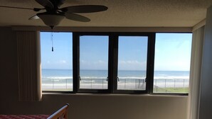 A bedroom with a bed, a ceiling fan, a window with a view of the beach, and a dresser. - Spacious Oceanfront 1st Floor 2 BR/2 BA Condo (Daytona Beach)