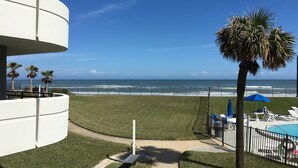 A view of a beach with a pool area, palm trees, and a clear blue sky. - Spacious Oceanfront 1st Floor 2 BR/2 BA Condo (Daytona Beach)