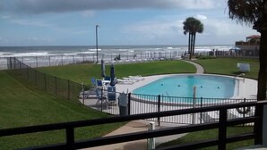 A pool area with a view of the ocean, surrounded by a fence and palm trees. - Spacious Oceanfront 1st Floor 2 BR/2 BA Condo (Daytona Beach)
