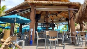 Un área de bar al aire libre con techo de paja, asientos y sombrillas.