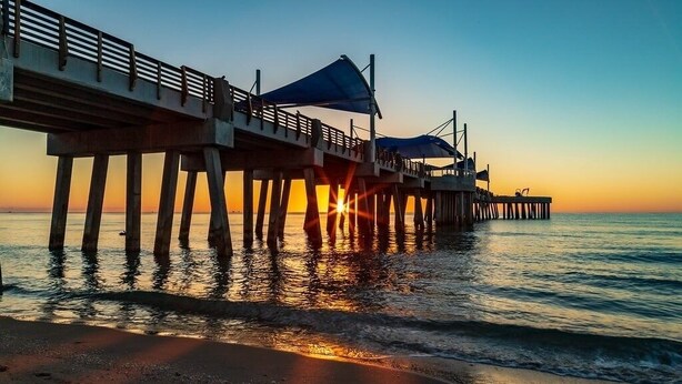Un muelle se adentra en aguas tranquilas al atardecer, bajo un cielo despejado.
